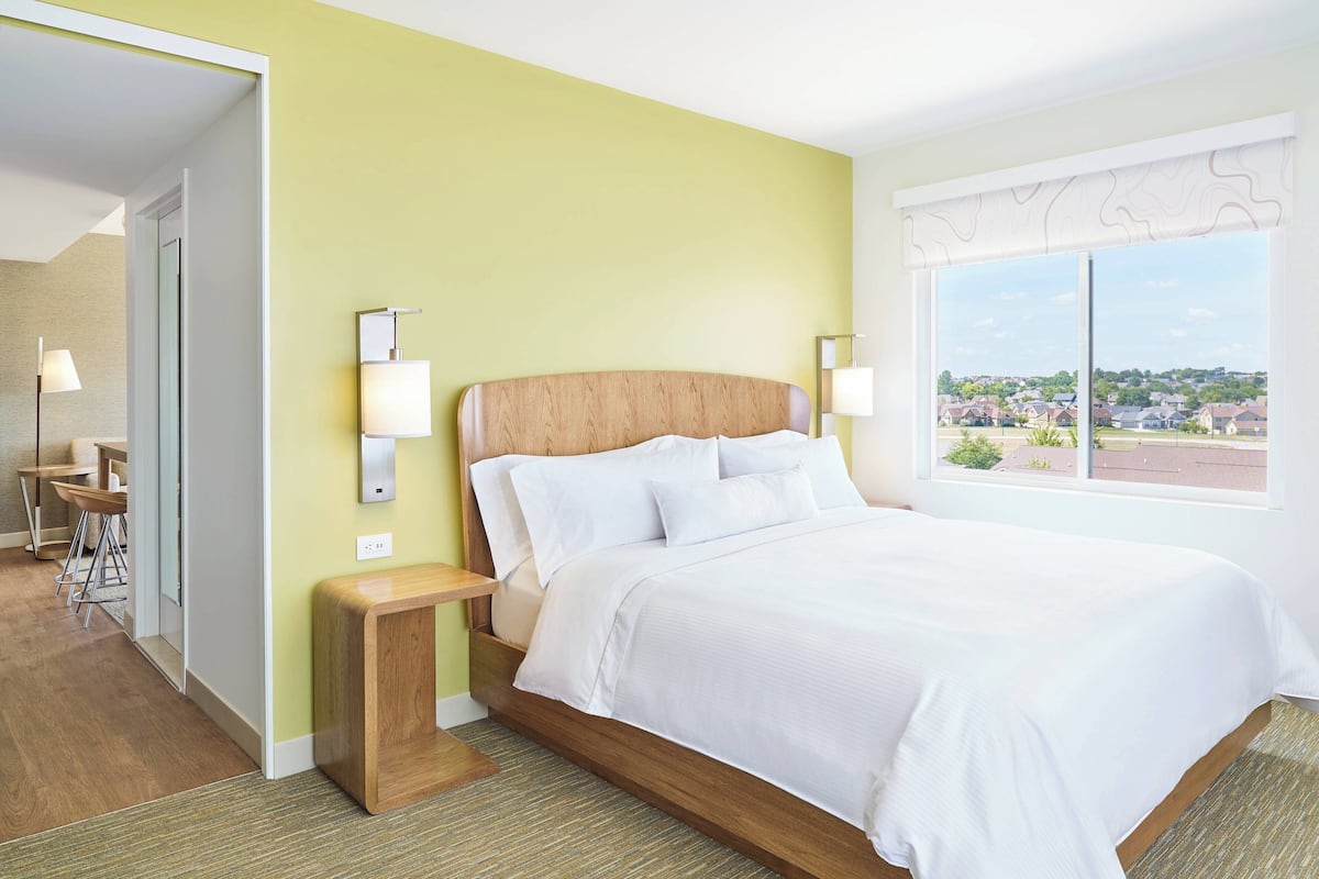 A hotel room with a bed, bedside lamps, a view of the outside, and a small seating area with chairs.