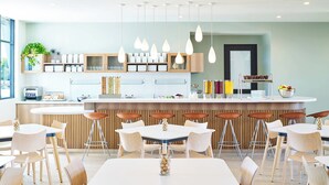 A modern restaurant with a central bar, white tables, and wooden chairs. - Element by Marriott West Des Moines (West Des Moines)