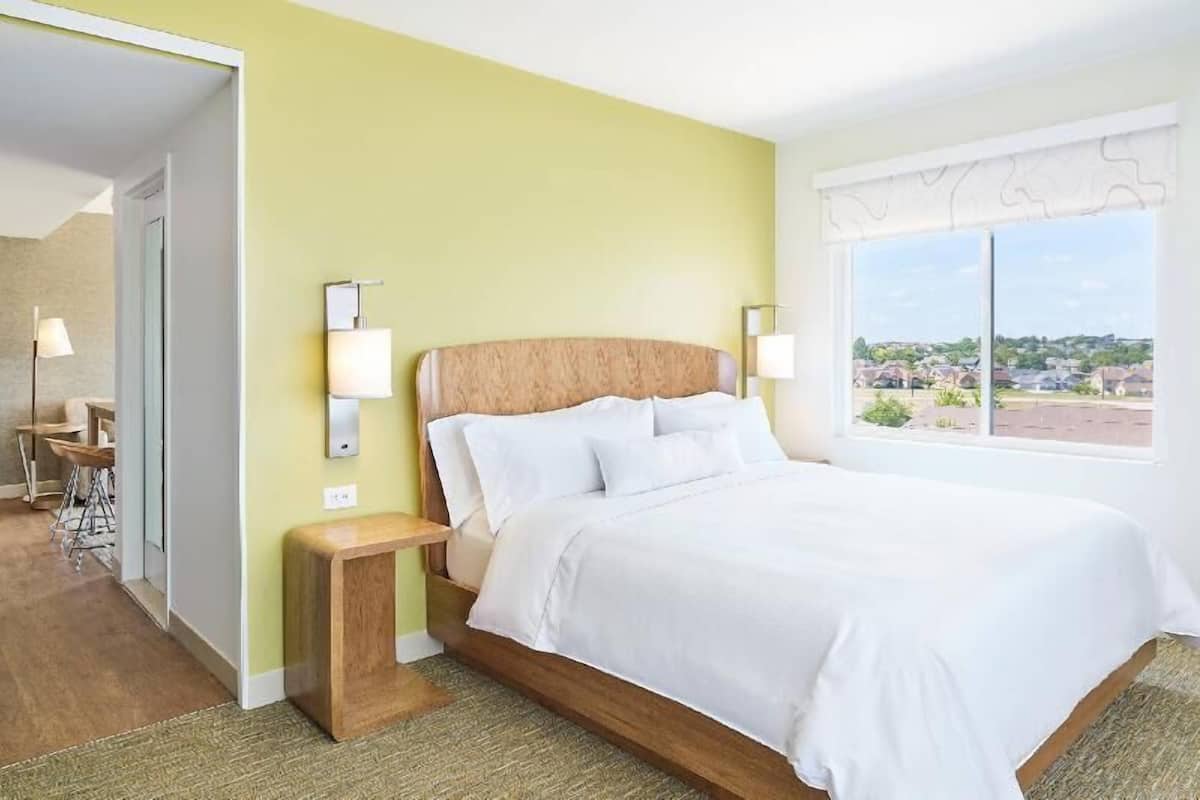 A hotel room with a bed, bedside lamps, a small table, and a window with a view.