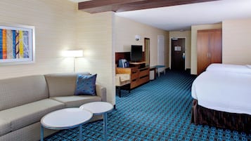 A hotel room with a sofa, two small tables, a TV, a desk, a wardrobe, and a patterned carpet.