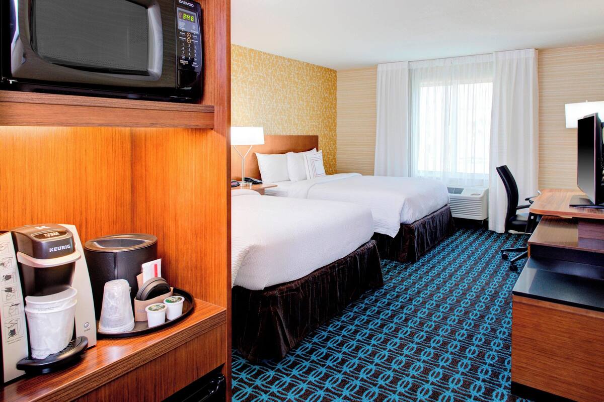 Ein Hotelzimmer mit einem Bett, einem Schreibtisch, einer Mikrowelle, einer Kaffeemaschine und einem Fernseher.