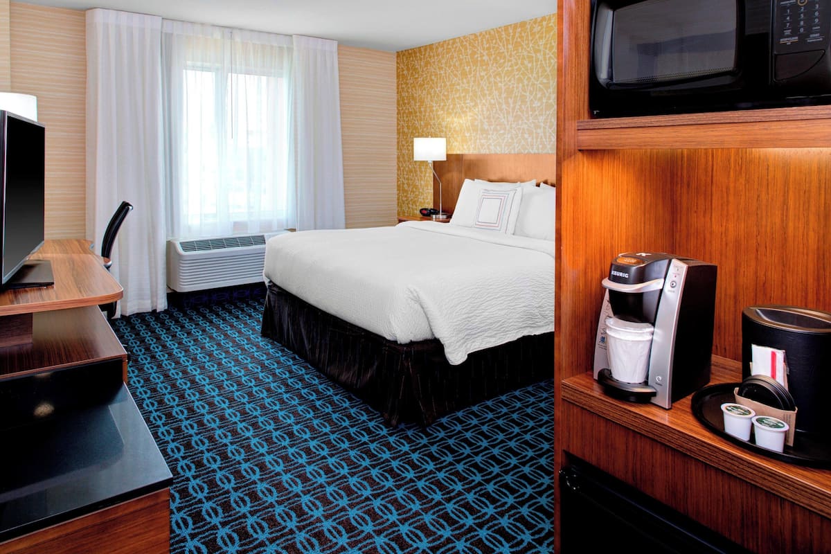 Ein Hotelzimmer mit Bett, Schreibtisch, Fernseher, Kaffeemaschine und Mikrowelle.