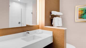 A modern bathroom with a large white sink, a mirror, and a toilet. There is a towel rack with folded towels and a framed artwork on the wall.