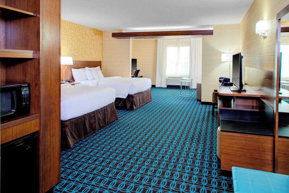 Ein Hotelzimmer mit zwei Betten, einem Schreibtisch, einem Fernseher, einer Mikrowelle und einem Badebereich.