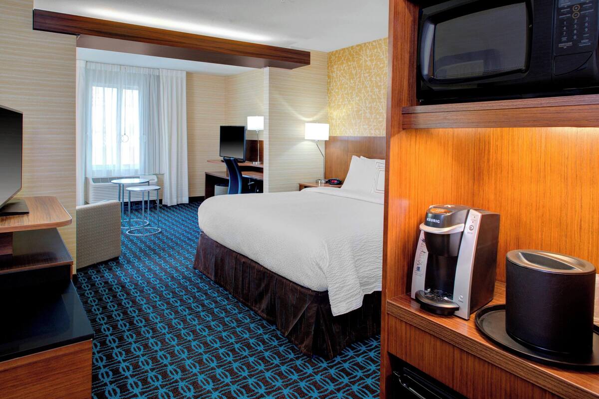 Ein Hotelzimmer mit einem Bett, einem Schreibtisch, einem Sessel, einem Fernseher, einer Mikrowelle und einer Kaffeemaschine.