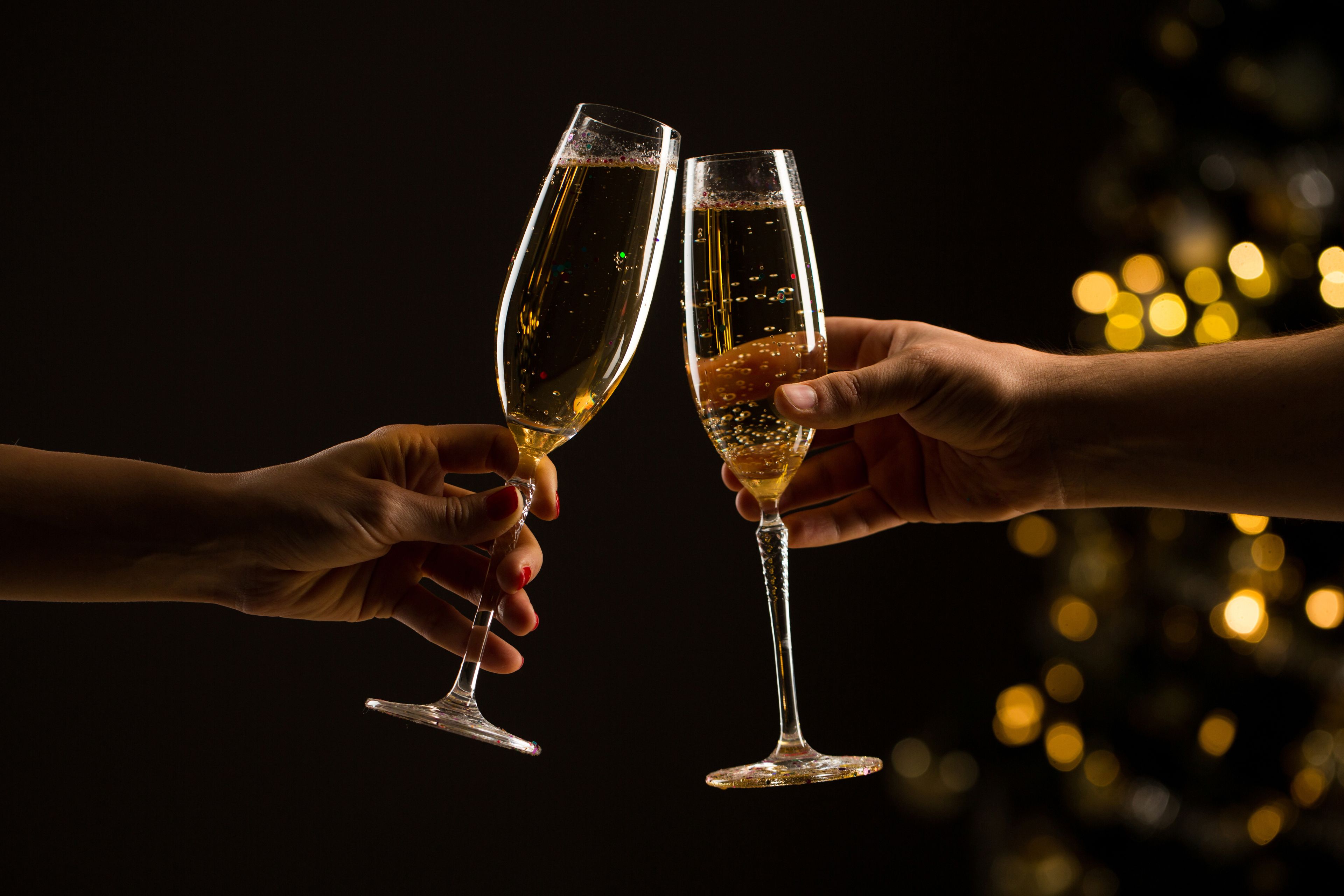 Two hands holding champagne flutes with a dark background and blurred lights.