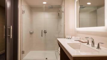 Ein modernes Badezimmer mit einer Glaskabine zur Dusche, einem großen Spiegel und einem Waschtisch mit zwei Becken und modernen Wasserhähnen.