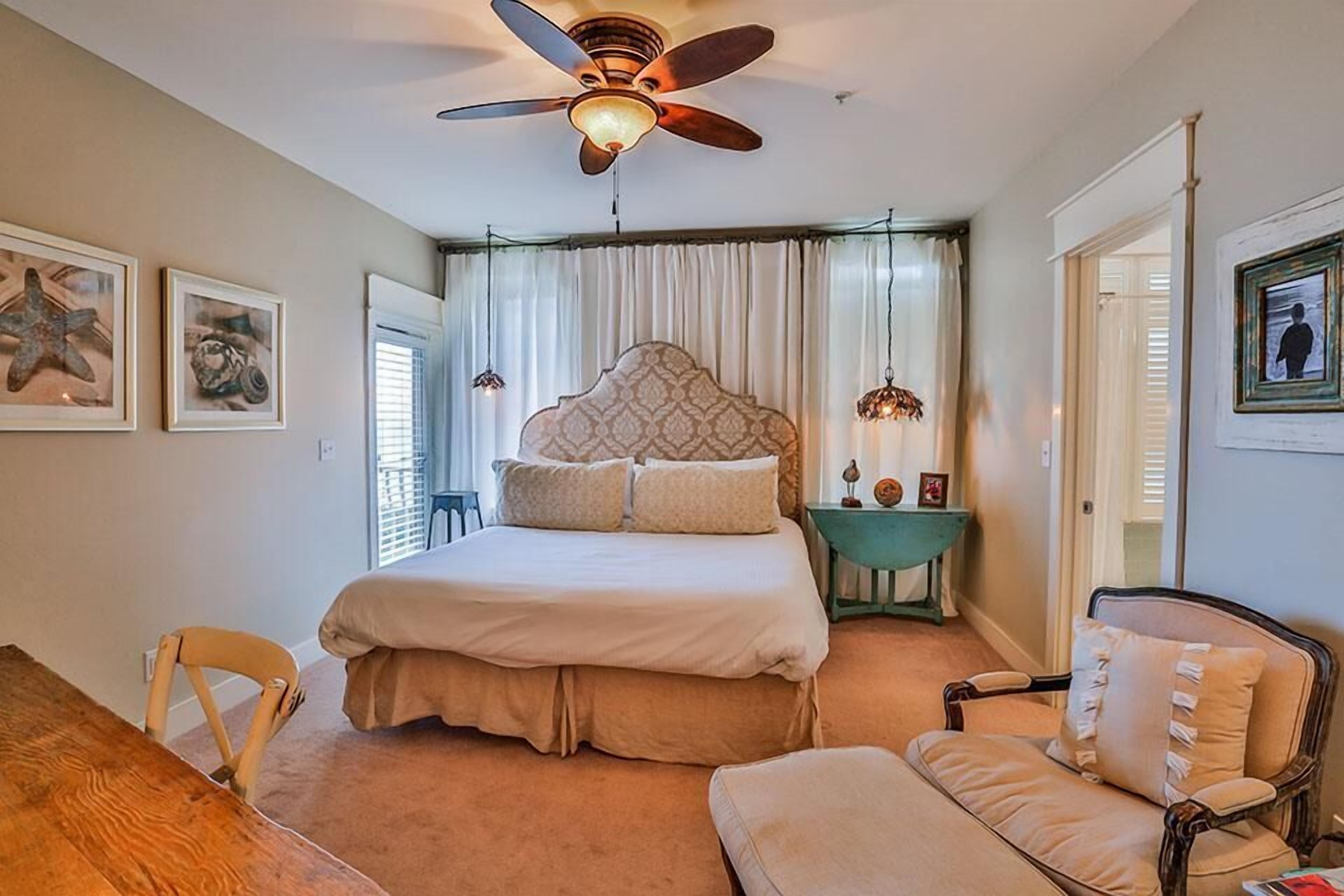 A bedroom with a large bed, a ceiling fan, a nightstand, a chair, and a desk.