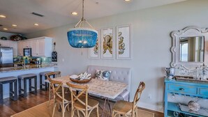 A dining area with a table and chairs, a chandelier, and a blue cabinet with decorative items. - 3 by the Sea 3 Bedroom Holiday Home by Five Star Properties (Panama City Beach)