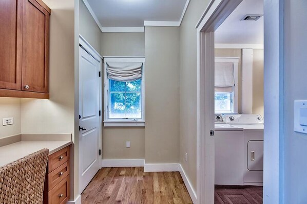 A laundry room with a washing machine and dryer, a window with a view of trees, and wooden cabinets.