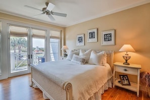 A bedroom with a bed, two bedside tables with lamps, a ceiling fan, and a balcony with a view.