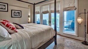 A bedroom with a four-poster bed, a ceiling fan, and a view of the outside balcony.