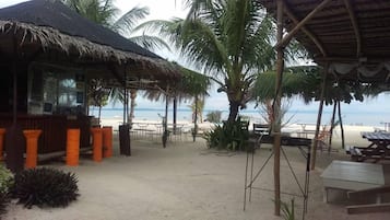 A beachside restaurant with outdoor seating, palm trees, and a view of the ocean.