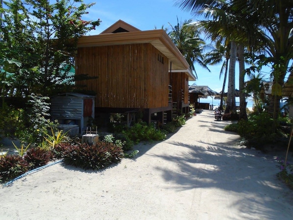 Un edificio de madera con techo de paja, rodeado de vegetación tropical y palmeras, lo que sugiere un entorno de resort.