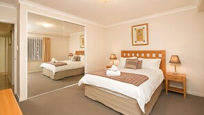 Habitación de hotel con dos camas, un espejo grande, lámparas de noche y un cuadro en la pared.