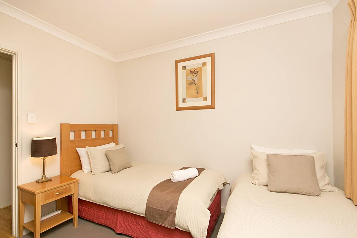 A hotel room with two beds, a nightstand with a lamp, and a framed picture on the wall.