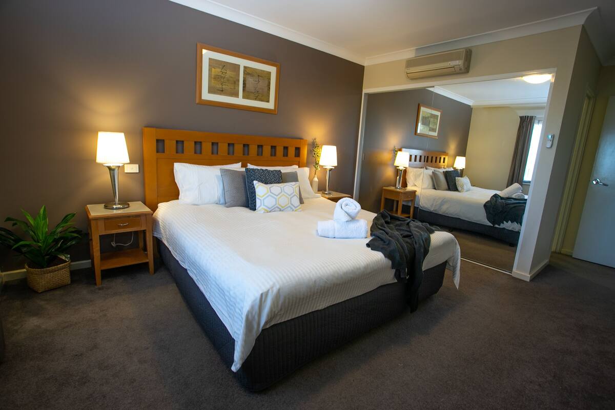 A hotel room with a large bed, two bedside tables with lamps, a potted plant, and a mirror.