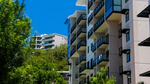 Un edificio residencial de varios pisos con balcones, rodeado de vegetación.
