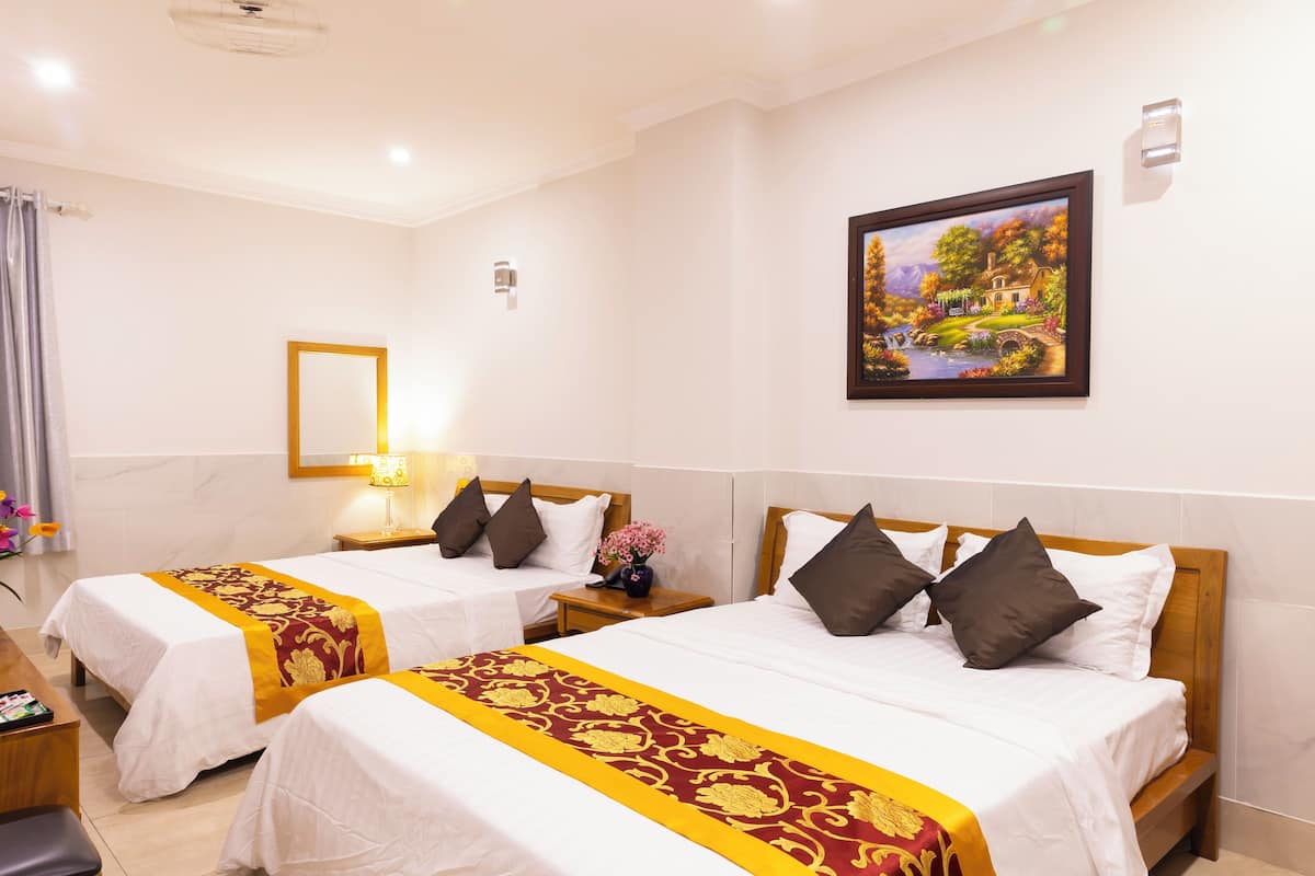 A hotel room with two beds, a wooden headboard, a nightstand with a lamp, a mirror, and a painting on the wall.
