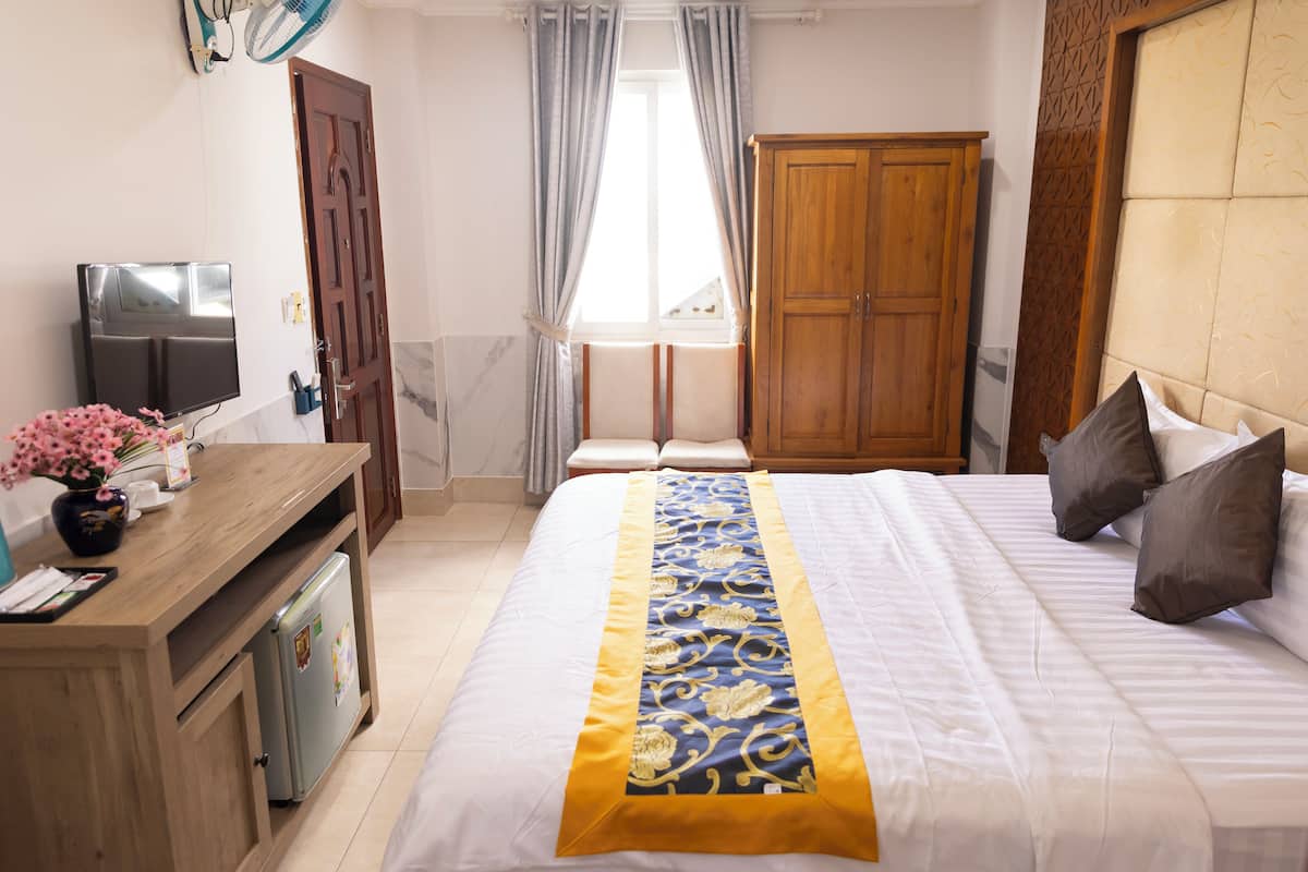 A hotel room with a bed, a wooden desk, a television, and a wardrobe.
