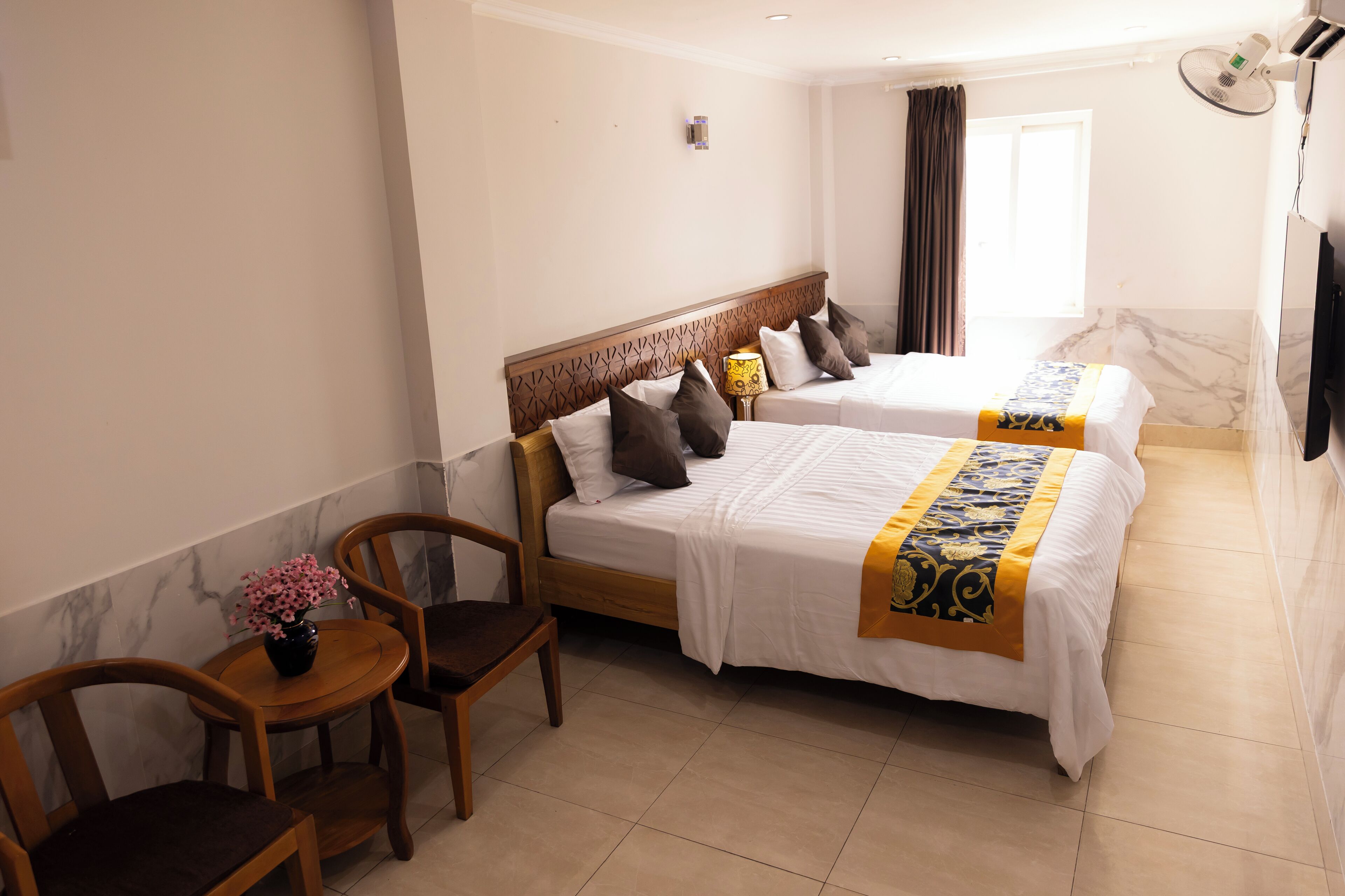 A hotel room with two beds, a small table with a vase of flowers, and a chair.