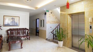A hotel lobby with a sofa, a staircase, an elevator, and a potted plant. - Atana Airport Hotel (Ho Chi Minh City)