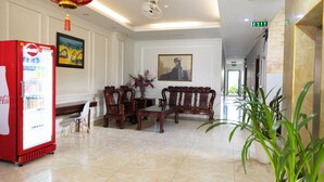 A lobby with a red Coca-Cola refrigerator, wooden furniture, a painting, and a potted plant. - Atana Airport Hotel (Ho Chi Minh City)