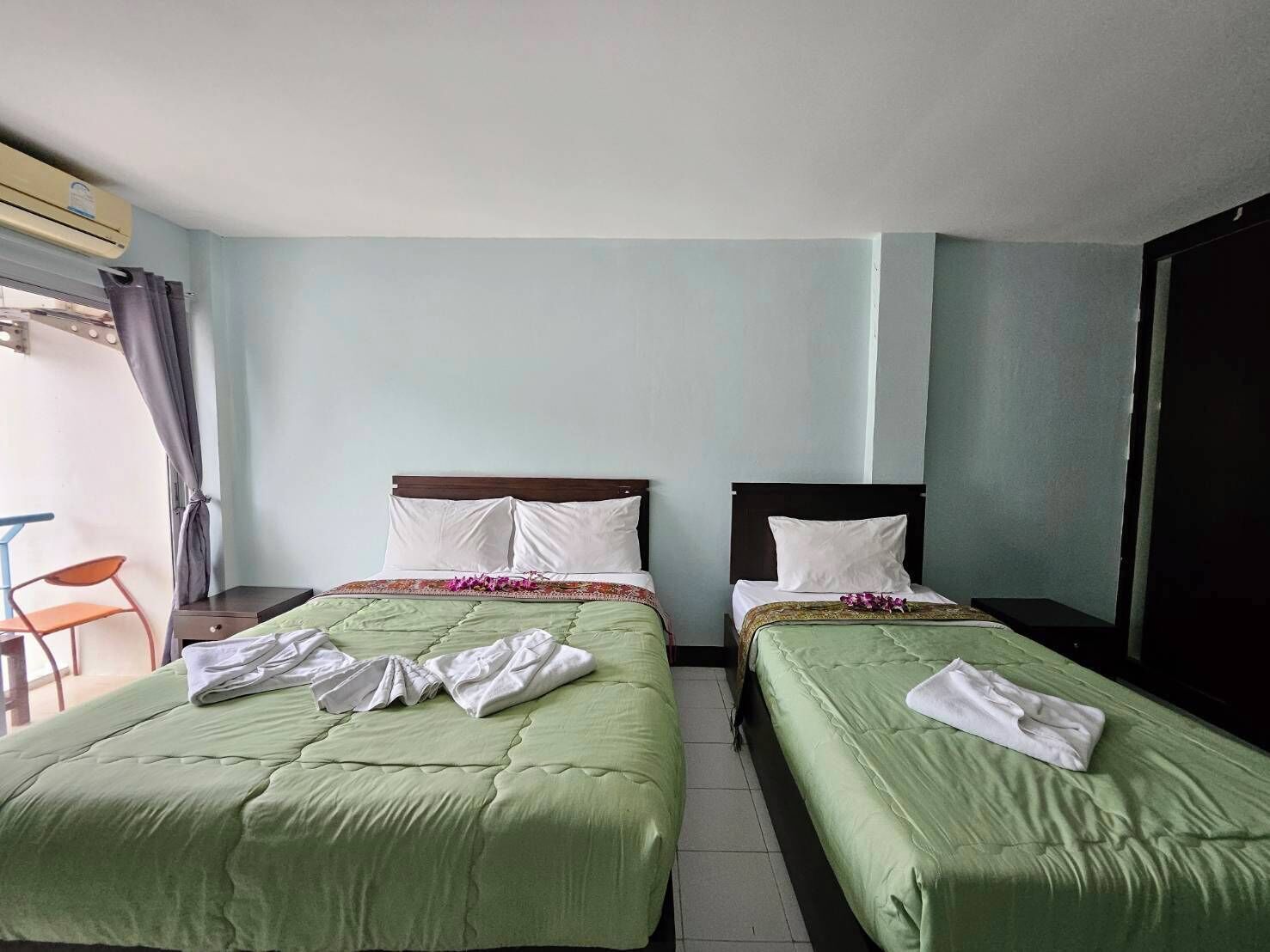Una habitación de hotel con dos camas individuales, una ventana con cortinas, una silla y un equipo de aire acondicionado.