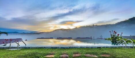 A serene lakeside view with a clear sky, calm water, and a grassy foreground with rocks.