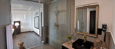 A modern bathroom with a glass shower enclosure, a black sink with a gold faucet, and a large mirror with a gold frame.