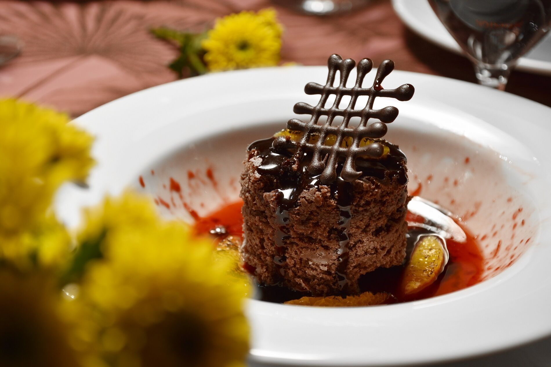 A dessert on a white plate with a decorative chocolate lattice on top, accompanied by a slice of lemon and a red sauce.