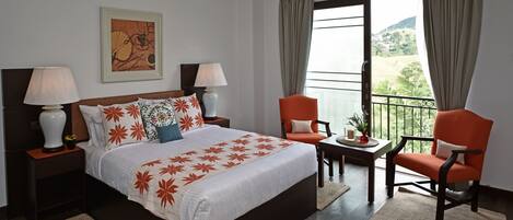 A hotel room with a bed, two nightstands, a table with a chair, and a balcony with curtains.