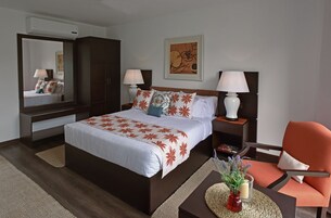 Habitación de hotel con una cama grande, dos mesitas de noche con lámparas, una silla, un espejo y un cuadro en la pared.