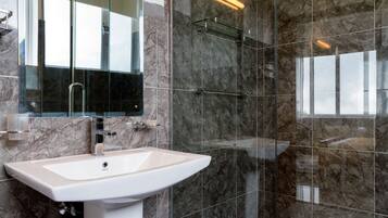 Un baño moderno con lavabo blanco, cabina de ducha de cristal y paredes de mármol.