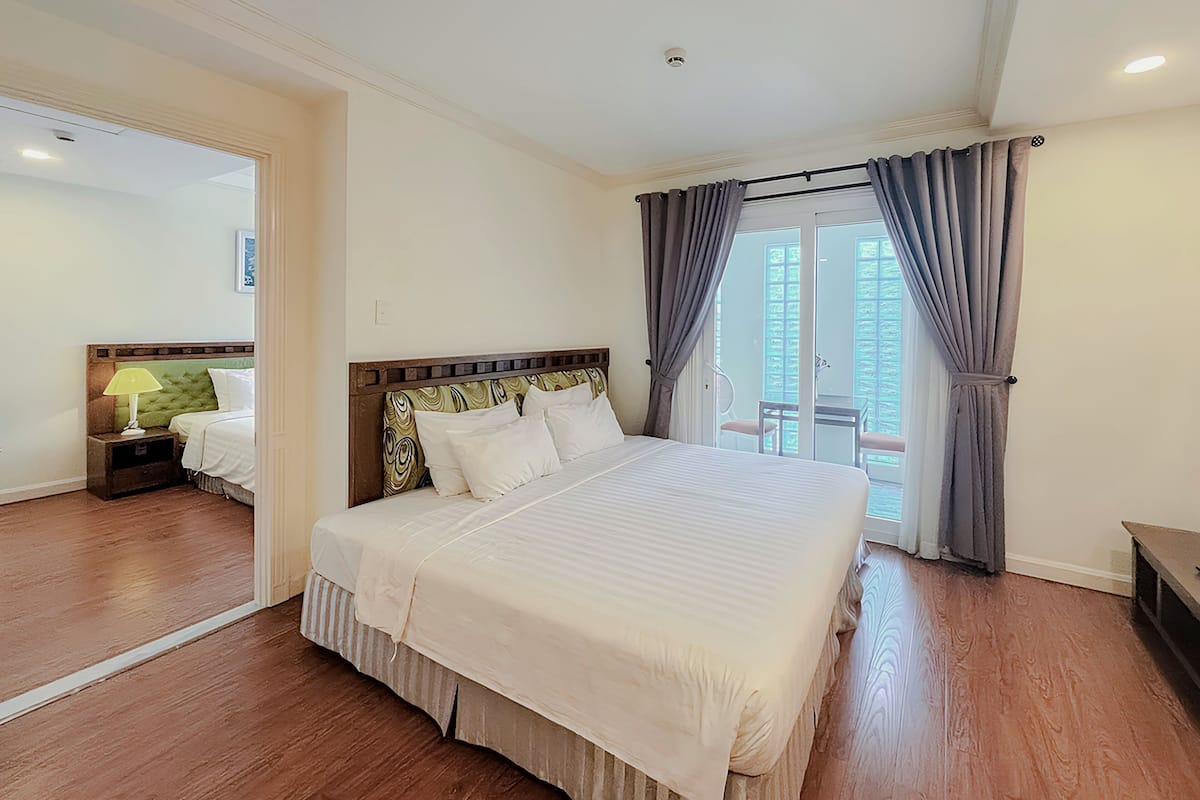 Une chambre d’hôtel avec un grand lit, une table de chevet, une lampe et une vue sur le balcon extérieur.