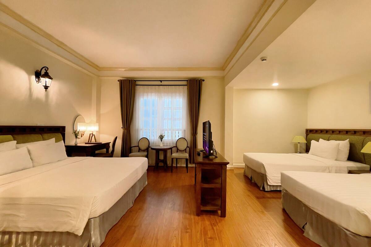 Une chambre d’hôtel avec deux lits, un bureau avec une chaise, une télévision et une fenêtre avec des rideaux.