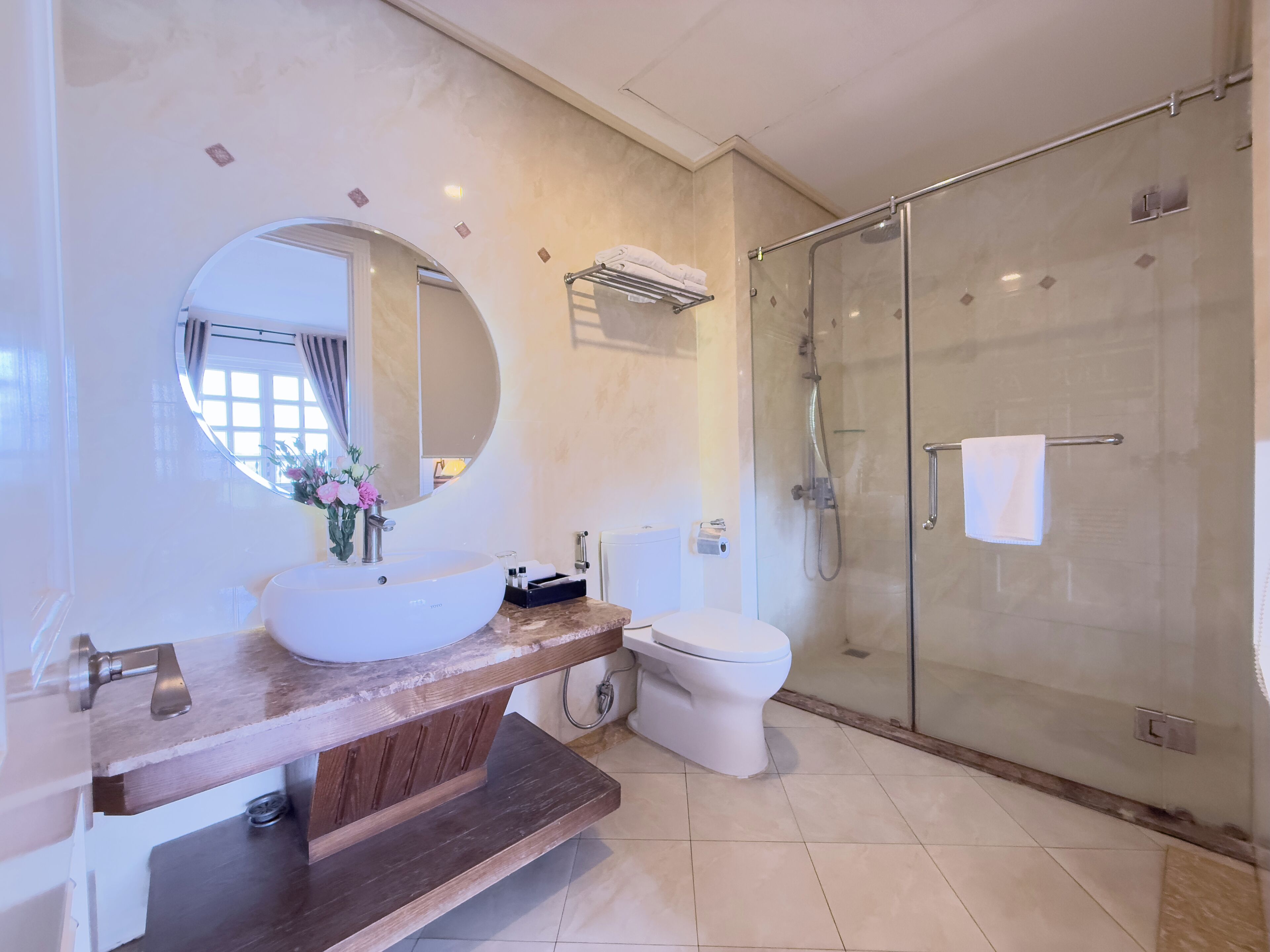 Un baño moderno con un espejo redondo, un lavamanos, un inodoro y una ducha con mampara de vidrio.