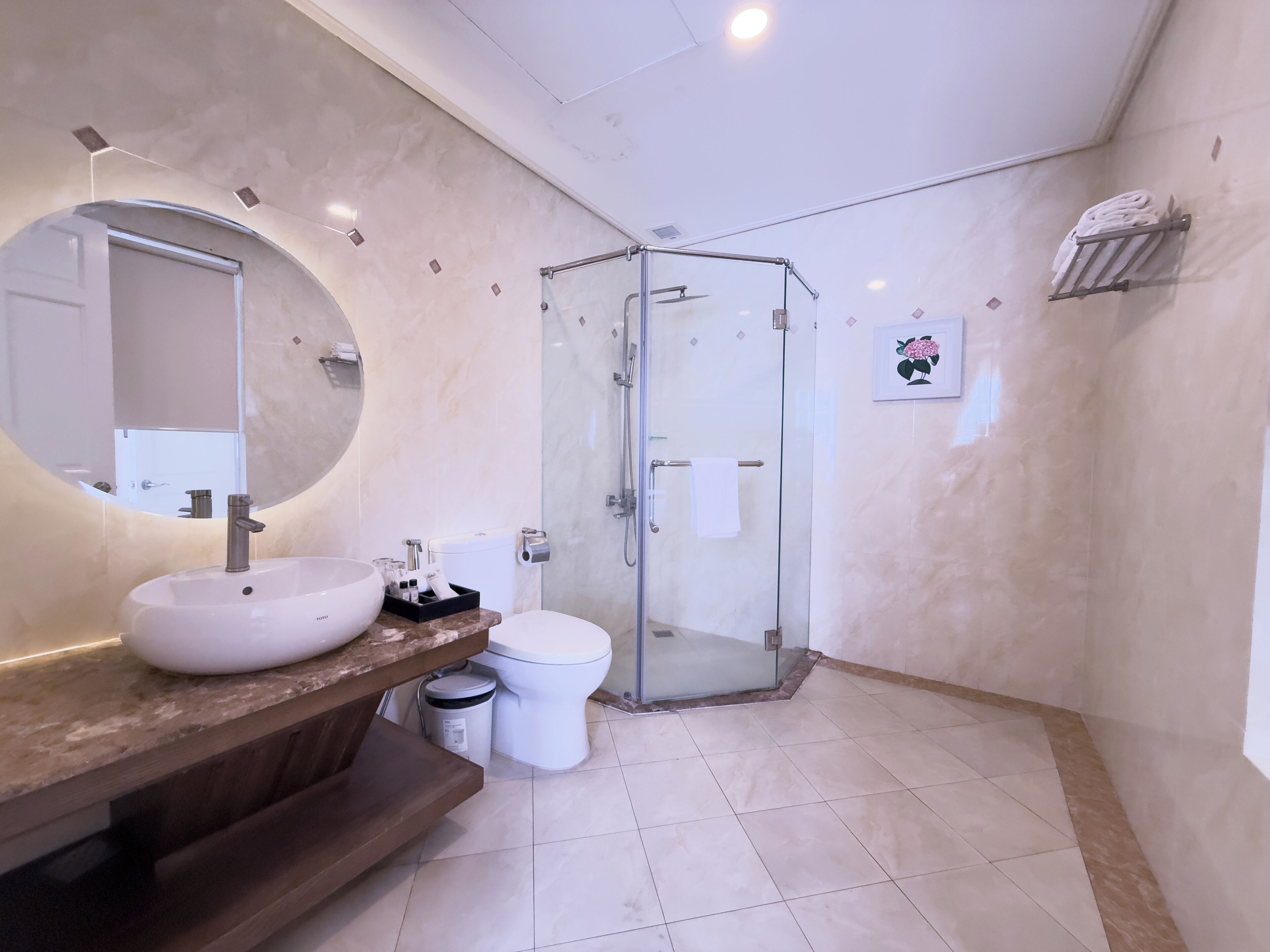 Et moderne badeværelse med et rundt spejl, en hvid vask, et toilet og en brusekabine med glasvægge.