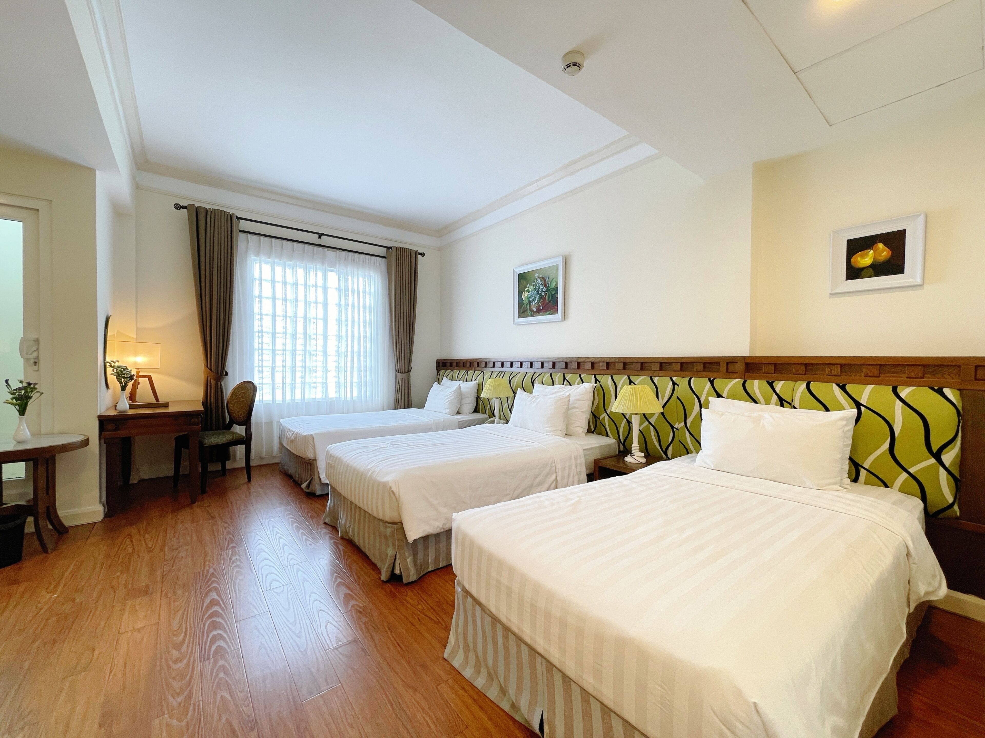 Une chambre d’hôtel avec deux lits, un bureau avec une lampe, une chaise et une fenêtre avec des rideaux.