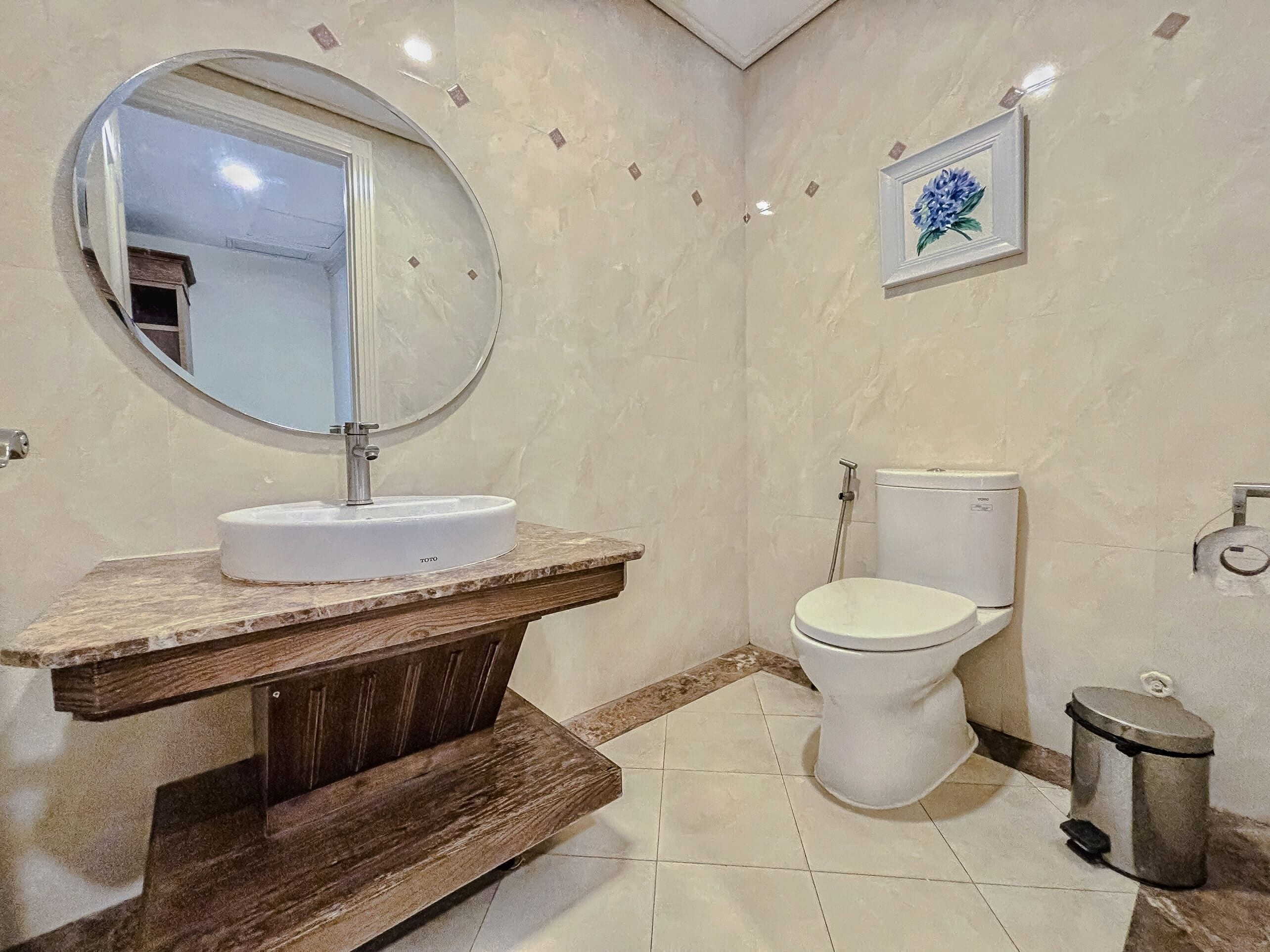 Une salle de bain avec un miroir rond, un lavabo blanc, des toilettes et une poubelle.