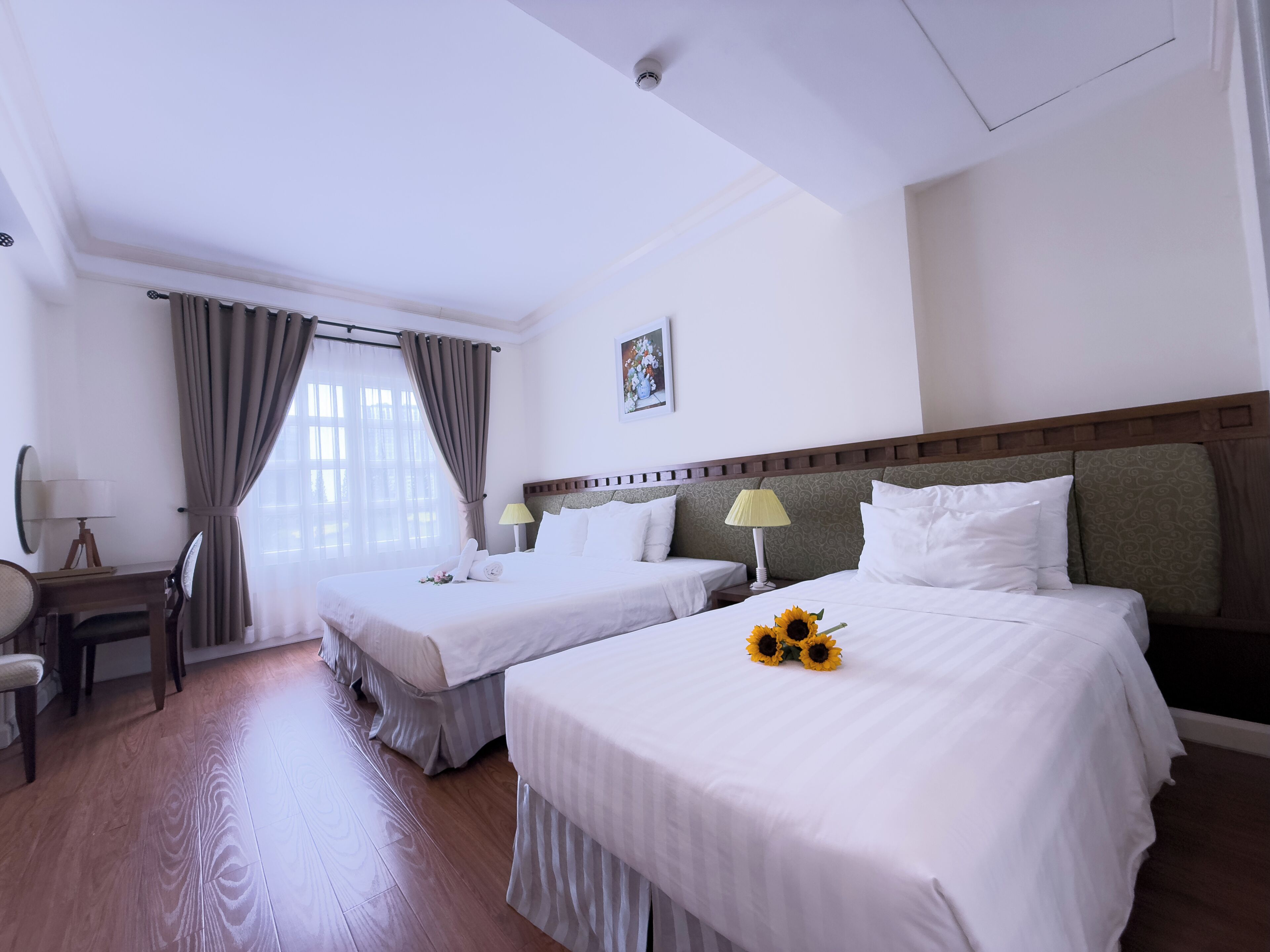 A hotel room with two beds, a desk, a chair, and a window with curtains.