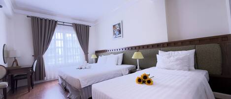 A hotel room with two beds, a desk, a chair, and a window with curtains.