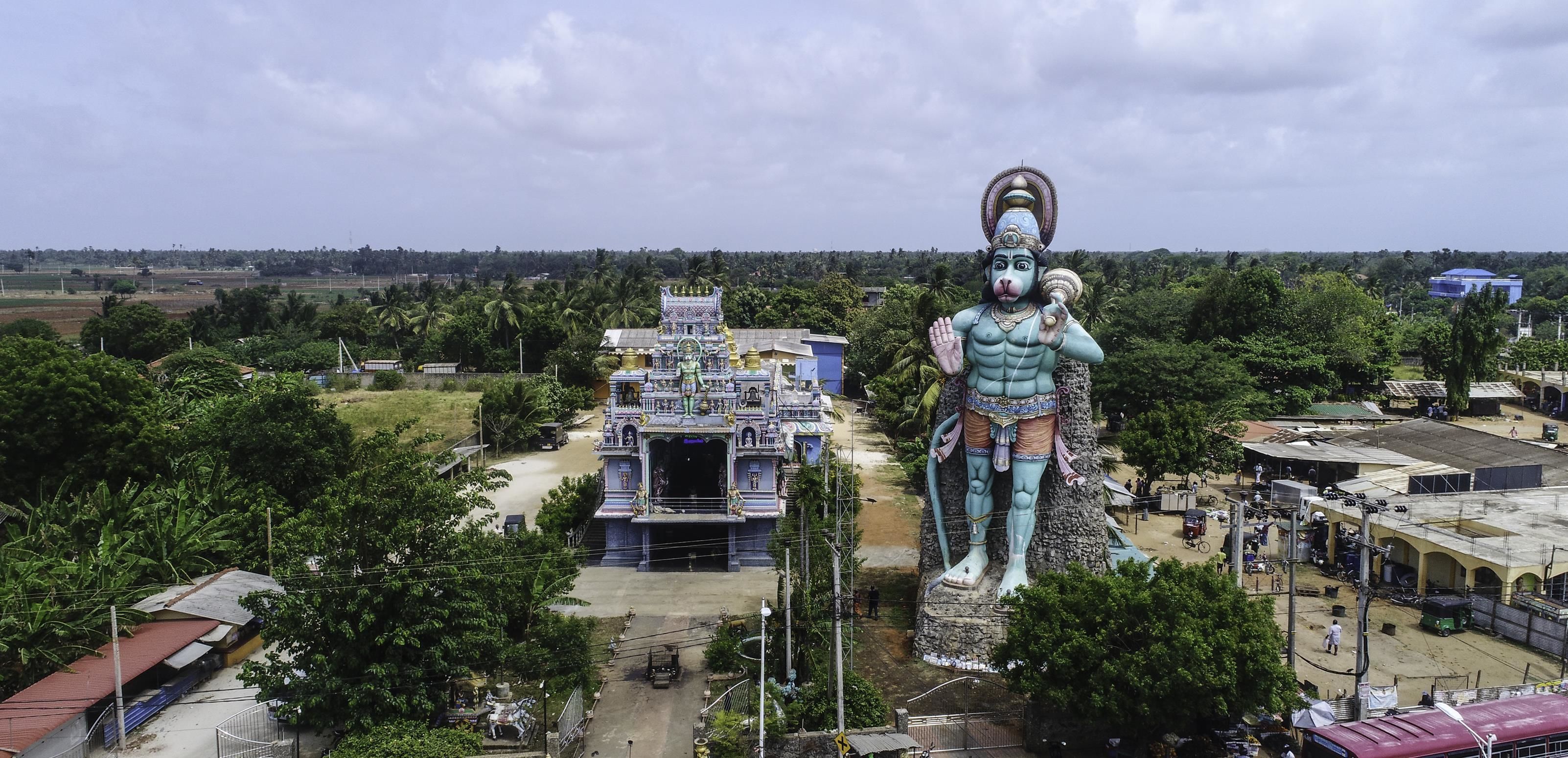 A large statue of a deity in front of a temple with a traditional architectural style.
