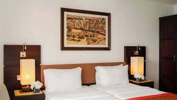 Una habitación de hotel con una cama grande, dos mesitas de noche con lámparas, una obra de arte enmarcada sobre la cama y un armario de madera.