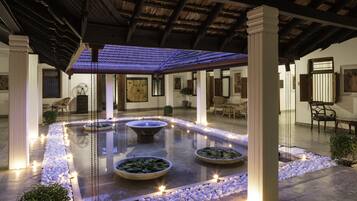 Relax in a serene courtyard with a central water feature, surrounded by pebbles and fountains, under a tiled roof.