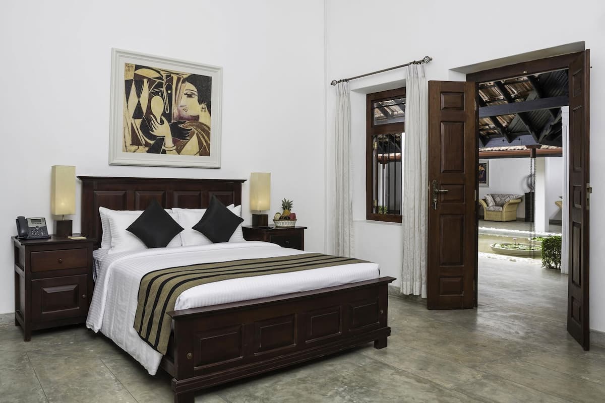A bedroom with a bed, bedside tables, a telephone, a lamp, a framed artwork, and an open door leading to a balcony.