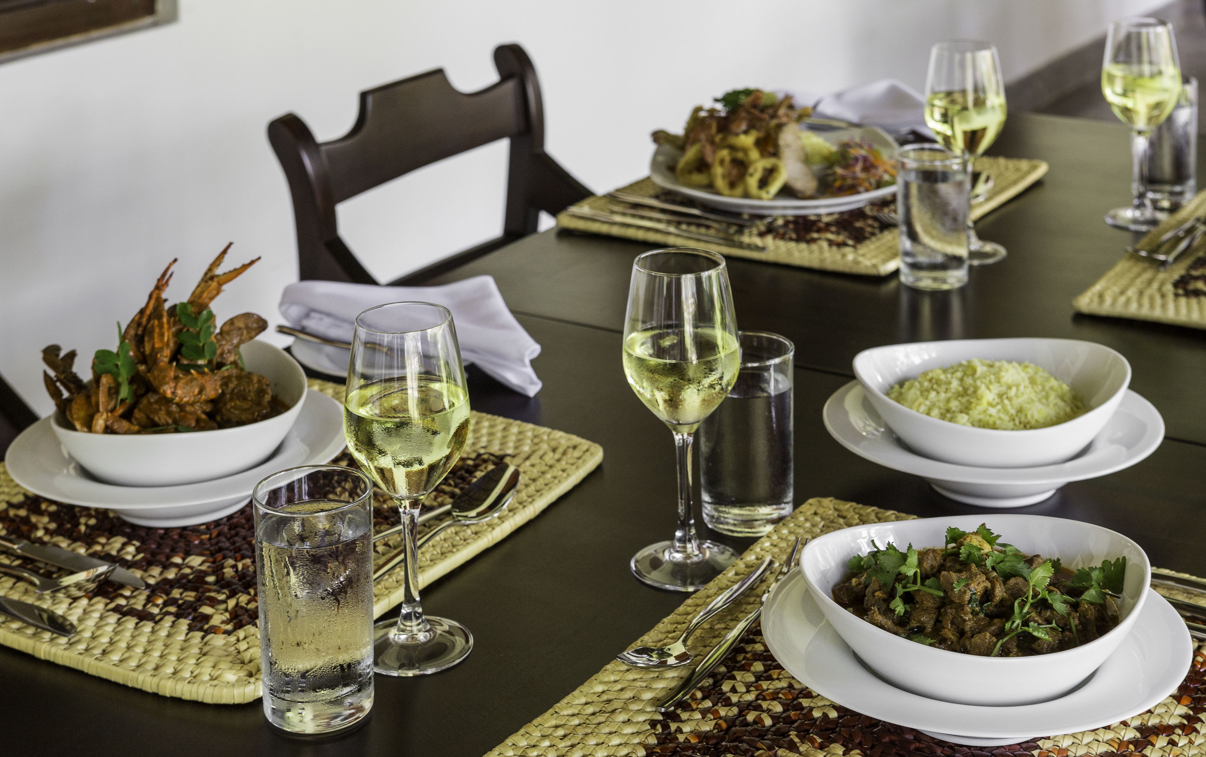 A dining table set with various dishes, glasses of white wine, and a bowl of rice.