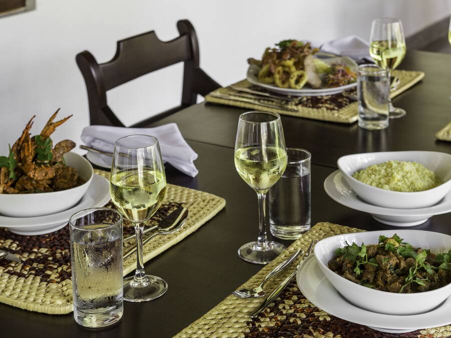 A dining table set with various dishes, glasses of white wine, and a bowl of rice.