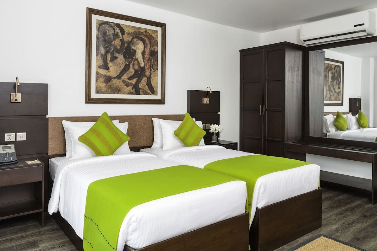 A hotel room with a large bed, a desk with a phone, a wardrobe, a mirror, and artwork on the wall.