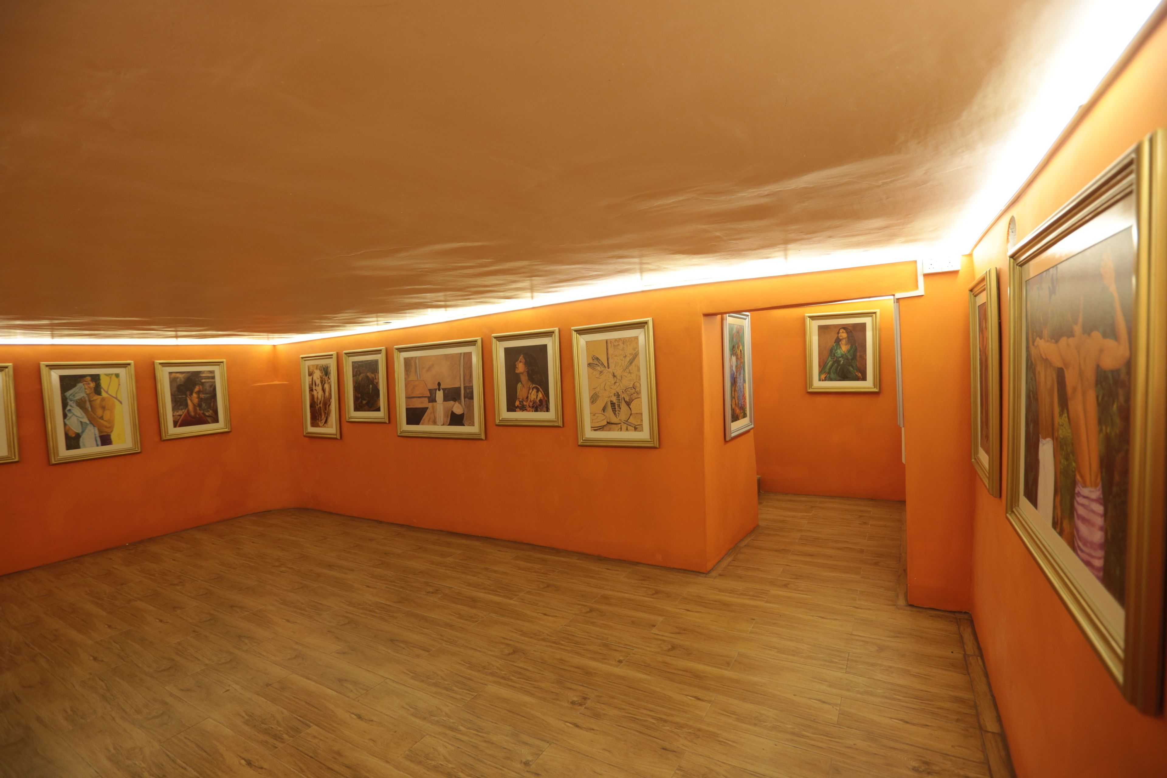 An art gallery with orange walls and wooden floors, featuring several framed artworks on display.